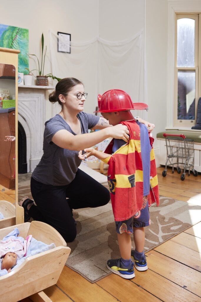 An adult woman helping a young boy put on a fireman costume