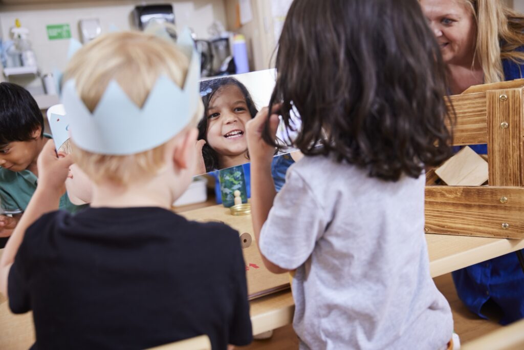 Group of kids playing with a mirror and toys with an adult close by