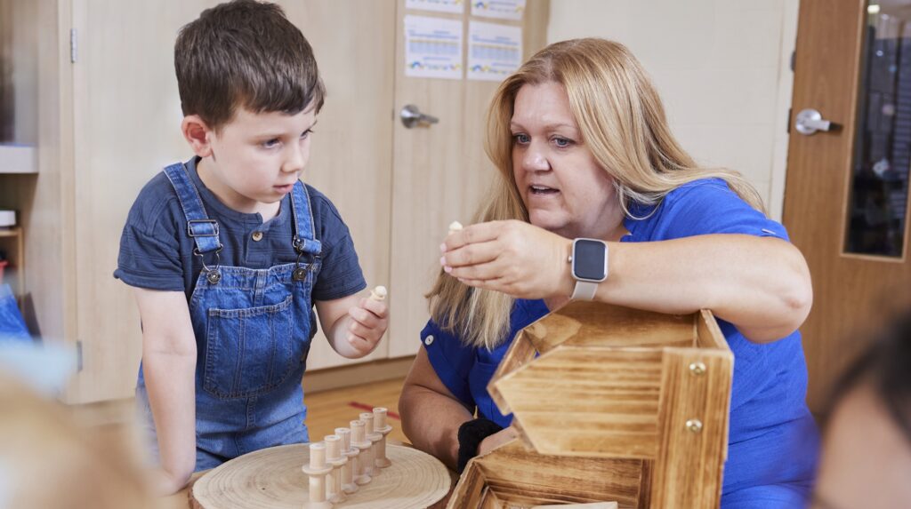 Adult woman showing young boy how to play with small wooden toys