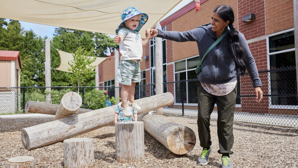 Young boy jumping on a playground with help from an adult.