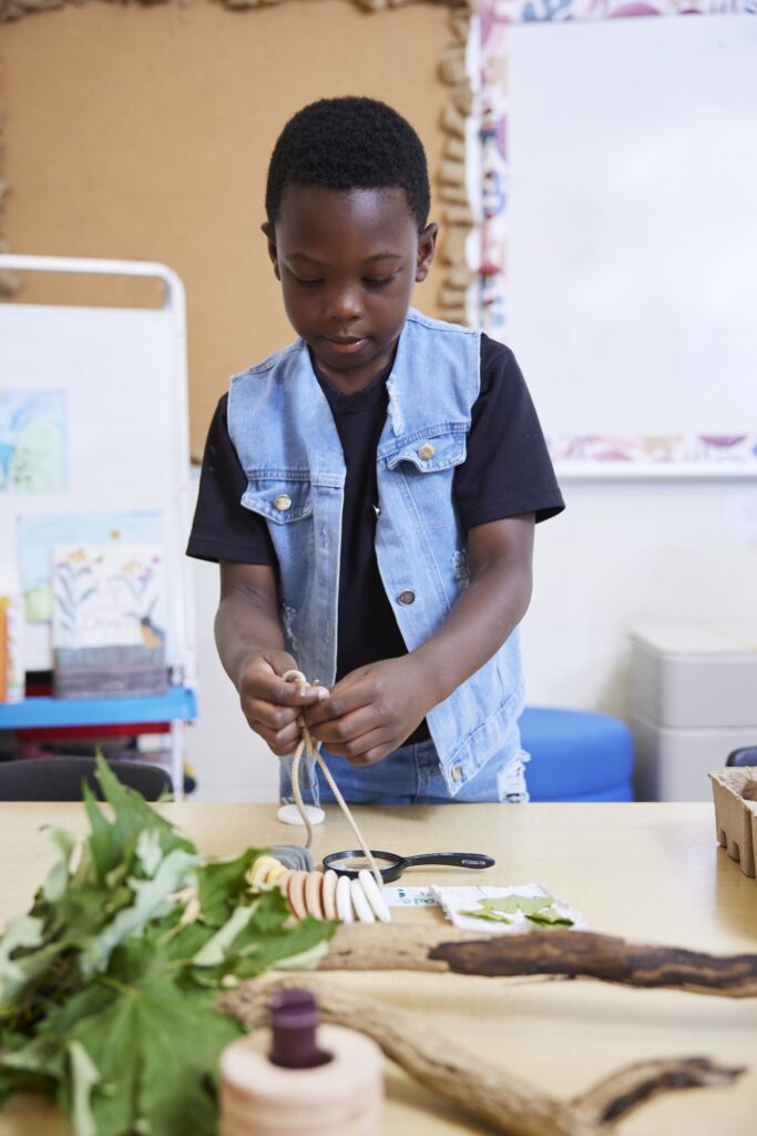 Young boy playing with rope and wooden toys with magnifying glass